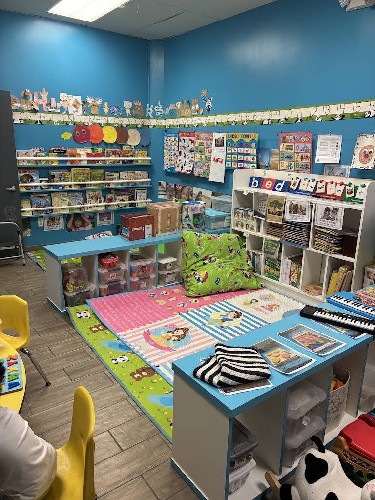 Bloom & Beyond's blue preschool classroom with books, learning shelves, and a colorful play rug
