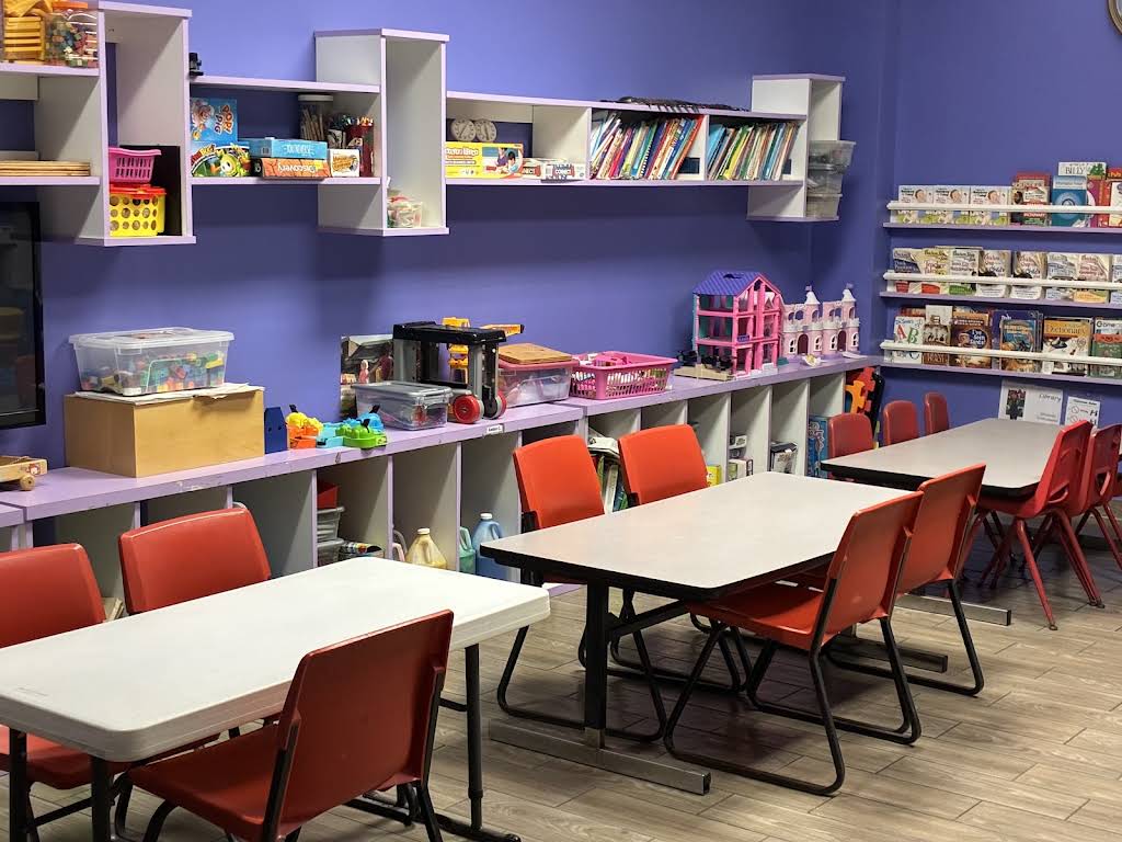 Bloom & Beyond's purple school-age classroom with activity tables, red chairs, books, and toys